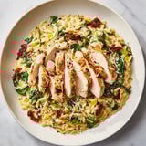 A close-up of golden-brown Marry Me Chicken Orzo with sun-dried tomatoes and fresh basil garnish.