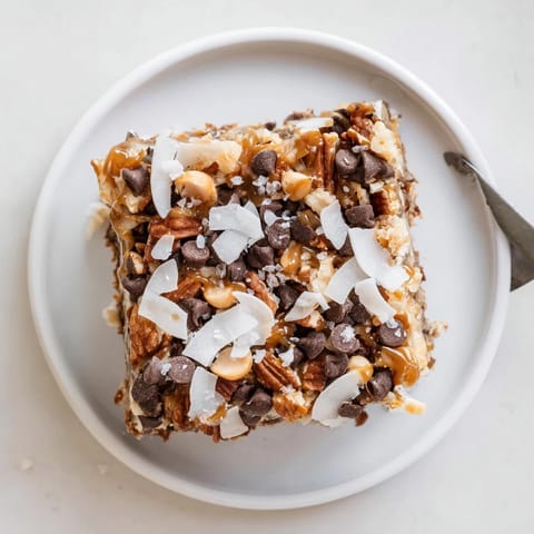 Chewy, homemade 7-Layer Magic Bars with visible chocolate chips and scattered pecans served.