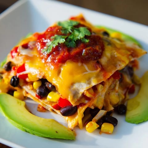 Cheesy layers of Quick Black Bean and Corn Tortilla Casserole, served with fresh cilantro and lime wedges.