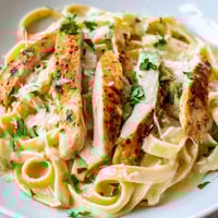 Creamy Cajun Chicken Alfredo pasta twirled on a fork with tender, spice-rubbed chicken strips and a glossy Parmesan sauce.